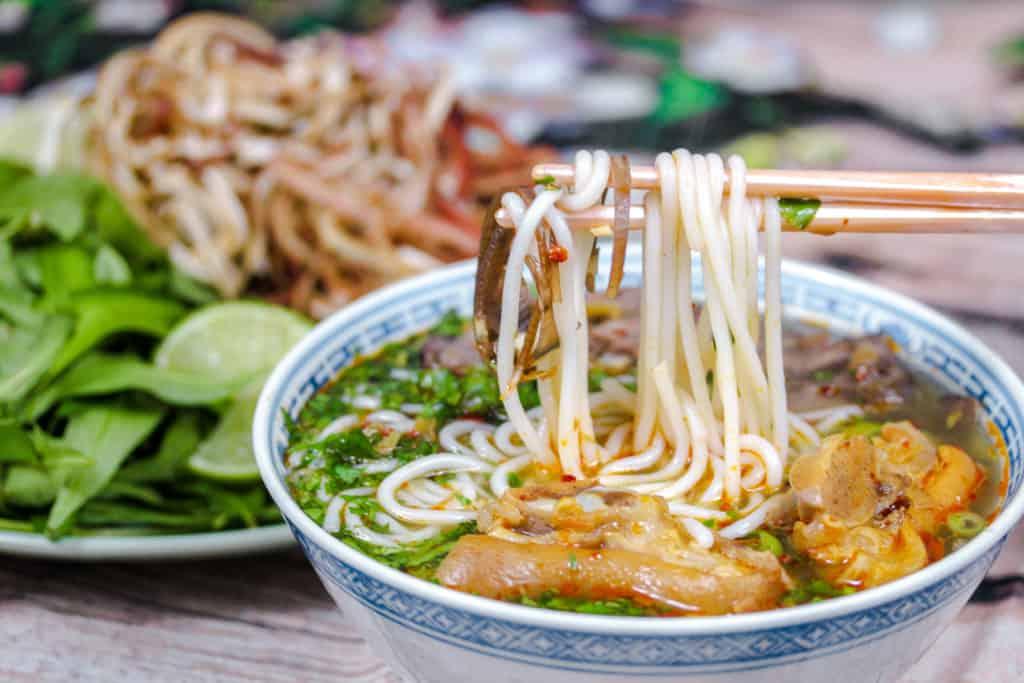 chopsticks lifting noodles out of a bowl of Spicy Vietnamese Beef Noodle Soup (Bún bò Huế)