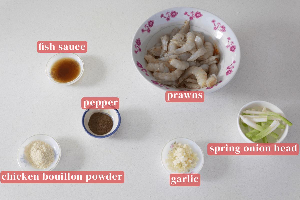 A bowl of prawns with dishes of fish sauce, pepper, chicken bouillon powder, minced garlic and spring onion heads.