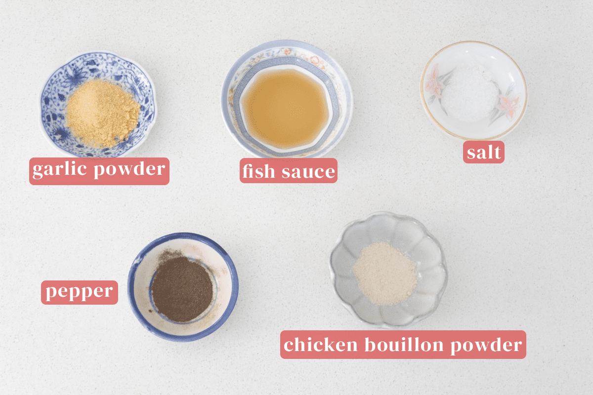 Dishes of garlic powder, fish sauce, salt, chicken bouillon powder and pepper.