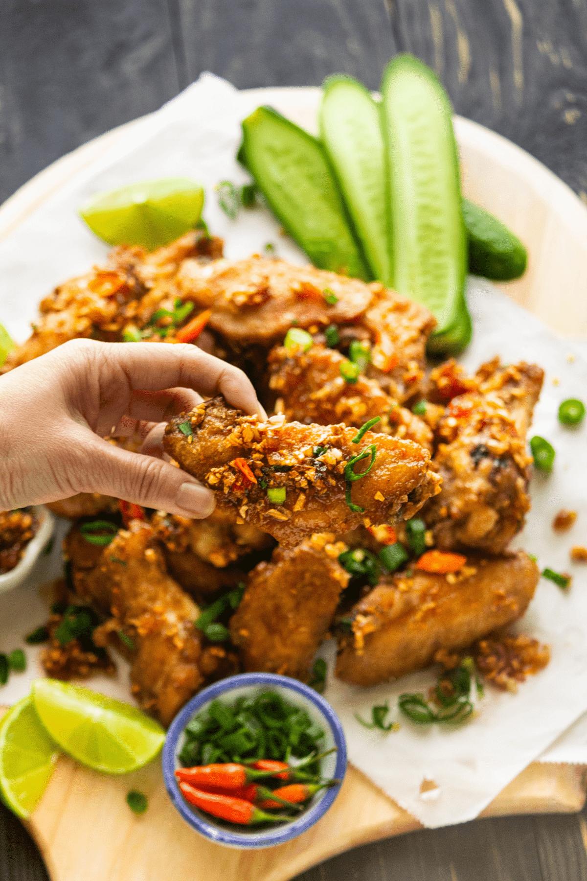 A hand holding a Fish Sauce Chicken Wing over a plate of fried wings.